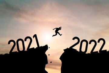 Welcome merry Christmas and happy new year in 2022,Silhouette Man jumping from 2021cliff to 2022 cliff with cloud sky and sunlight.
