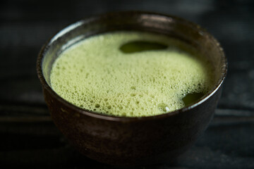 Top view of Japanese organic matcha green tea powder in bowl on black wooden surface. Healthy product from the nature typical of the Japanese tradition. Tea ceremony concept.