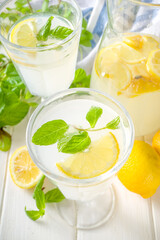 Iced homemade lemonade drink, limoncello liqueur cocktail decorated with mint and lemons on white wooden kitchen background