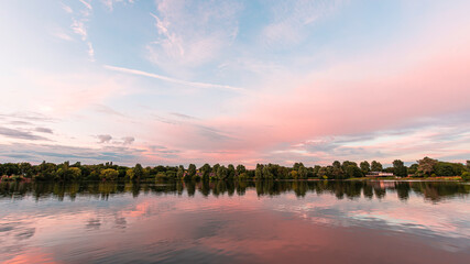 Sunset over Westport lake in Stoke on Trent, Staffordshire, UK.Reflection of blue sky and pink clouds on a calm water surface.Bright landscape scenery with pastel colours.Tranquil nature scene.