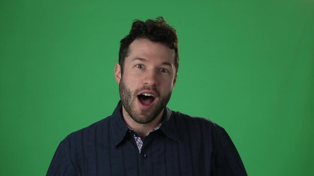 Slow motion portrait of amazed man shocked, saying WOW. Handsome hip guy with stylish hairdo surprised to camera on green screen chroma key background.