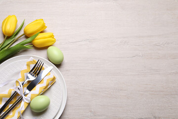 Festive Easter table setting with eggs and flowers on light wooden background, flat lay. Space for...