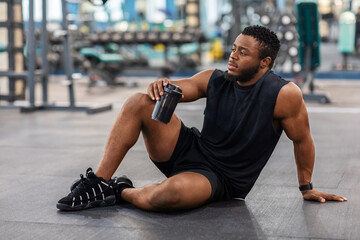 Fototapeta na wymiar Handsome black bodybuilder with water sitting on floor