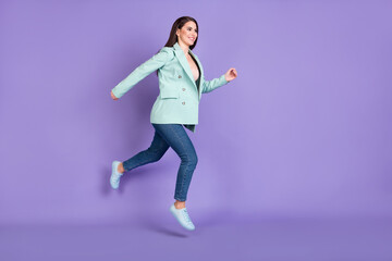 Fototapeta na wymiar Full size profile side photo of young lady jump go empty space wear teal jacket jeans isolated on violet color background