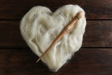 Heart shaped pile of white wool and spindle on wooden table, top view