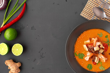 Tom yam Thai soup in black bowl served on gray background