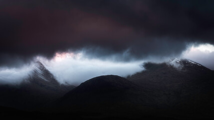 Naklejka na ściany i meble Extreme weather conditions in Scottish Highlands at dawn.Dark clouds over mountain peaks and cloud inversion in the valley.