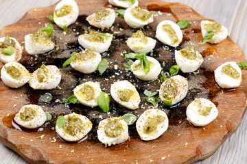 Mozzarella pieces with pesto, basil and olive oil on wooden rustic board.