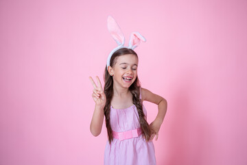 Beautiful little girl dressed in easter bunny ears and in a dress on a pink background.