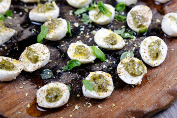 Mozzarella pieces with pesto, basil and olive oil on wooden rustic board.