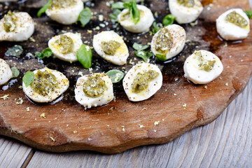 Mozzarella pieces with pesto, basil and olive oil on wooden rustic board.