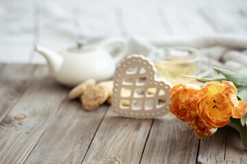 Spring home composition with a cup of tea, a teapot, cookies and a bouquet of flowers on a wooden surface.