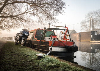 Motorbike parked next to narrow canal house boat side of river as sun rises.  Peaceful and idyllic with calm still water and reflections at dawn.