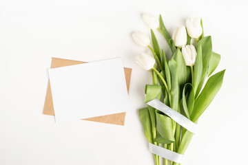 Fresh cut white tulip flowers and blank card with envelope top view on white background with copy space