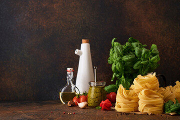Homemade tagliatelle pasta in brown paper on white background with olive oil, sause pesto, basil and garlic on light table background.