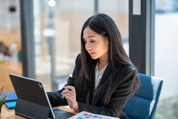 Obraz premium Asian businesswoman working on a tablet with documents at the desk in the office.