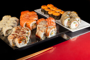 Sushi Sets Uramaki, California, Philadelphia, on a white plate. Festive new year concept. Against a dark reflective background.