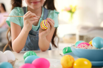 Little girl painting Easter eggs at table indoors, closeup
