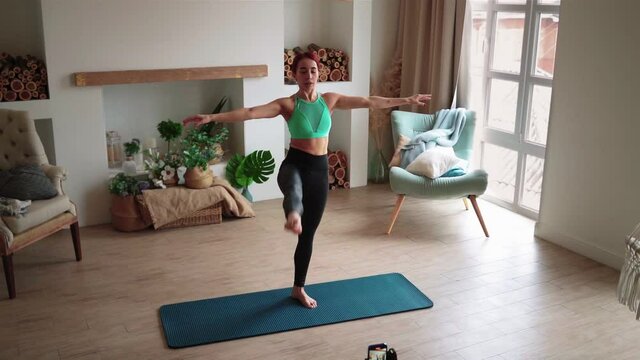Young Slim Woman Blogger Conducts a Fitness Lesson Online, Taking Pictures on a Mobile Phone. Coach Blogger Leads a Stretching Workout at Home. Video Blogging Concept. Live Streaming. Slow motion
