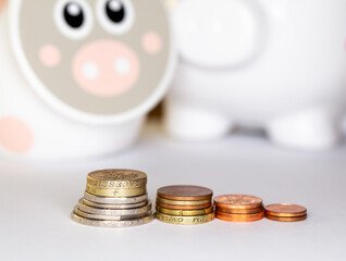 White porcelain piggy bank and a large amount of small coins. Object illuminated by artificial light, low angle