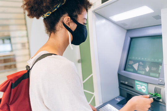 Young woman wearing face mask, using ATM