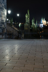 street lighting lantern on a stone tower on Charles Bridge and stone paving at night in the center of Prague