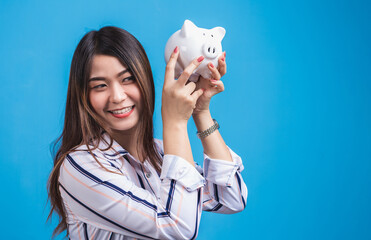 Fototapeta na wymiar Smiling happy young woman holding a piggy bank in blue background.