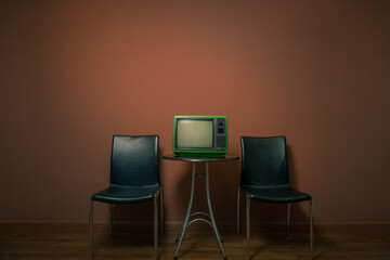 Retro old green TV on round table with chairs in front of the wall in a vintage room