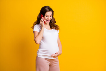 Portrait of pretty cheerful pregnant girl calling friend discussing childbirth isolated over bright yellow color background