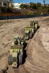 Earthmoving vehicles following each other while scrapping dirt  as part of a grading project on a...
