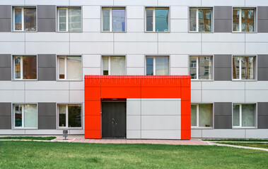 The wall of the building with a bright red entrance and bizarre reflections in the windows