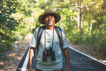 Portrait Asian old man hiking with binoculars and backpack in the forest.