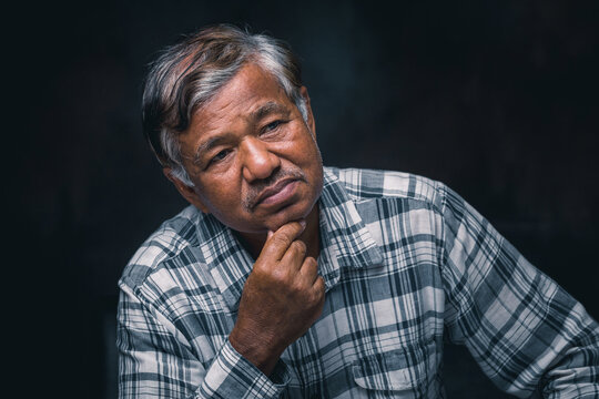 Portrait of sad old man in a plaid shirt on black background, taking a photo in studio
