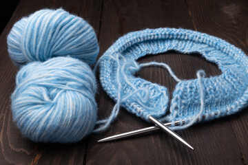 knitting needles, blue yarn and skeins on a dark wooden background