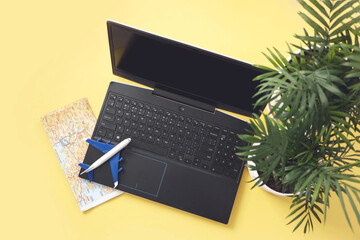 Laptop, model plane, map and leaves of palm on yellow background. Summer holiday, vacation, online booking, planning travel concept. Flat lay, top view.
