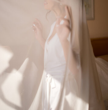 blurred image of the bride, who stands at the onk behind a white curtain