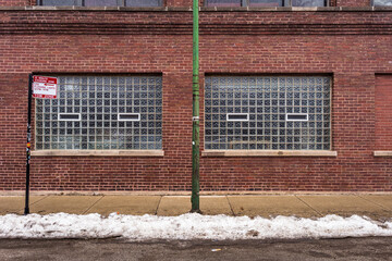 Fototapeta na wymiar Side of vintage red brick industrial building with snow on street and frosted windows in urban Chicago