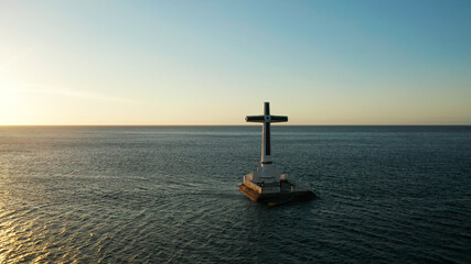 Catholic cross in sunken cemetery in the sea at sunset, aerial drone. Large crucafix marking the underwater sunken cemetary, Camiguin Island Philippines.