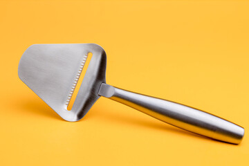 Shiny reflective stainless steel cheese slicer. Studio still life kitchen utensil against a seamless yellow background.