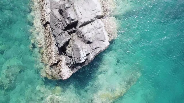 Aerial view of turquoise waves hitting stones. Shooting from a drone the surface of the water in the rays of the sun.