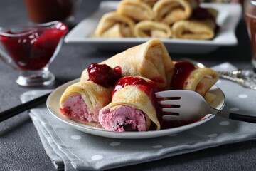 Homemade pancakes with curd filling and cherry, served with cherry sauce on a plate on dark background. Closeup