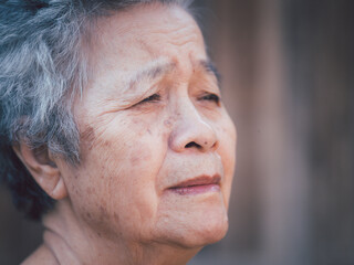 Senior woman with short gray hair, looking away and the face of worried while standing outdoors with wooden wall background. Side view. Space for text. Concept of aged people and healthcare