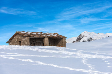 Old stone cow shed on the Lessinia Plateau (Altopiano della Lessinia) Regional Natural Park, in winter with snow. on background the peak of Monte Carega. Veneto, Trentino Alto Adige, Italy, Europe.