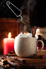 Obraz na płótnie Canvas still life with a full mug of hot chocolate and marshmallows. cinnamon is poured from the sieve onto the marshmallows