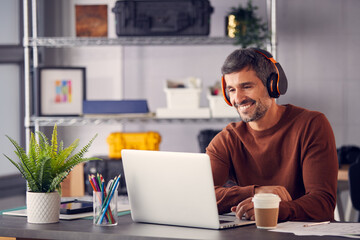 Male Advertising Marketing Or Design Creative With Wireless Headphones At Desk Working On Laptop
