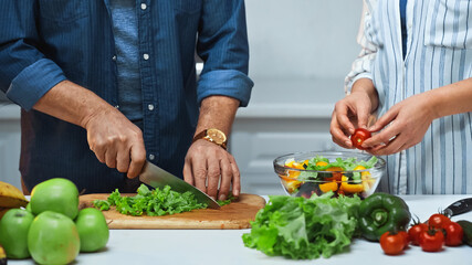cropped view of elderly couple preparing fresh salad in kitchen