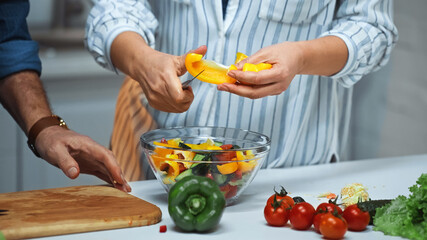 Obraz na płótnie Canvas partial view of senior woman cutting bell pepper near husband in kitchen