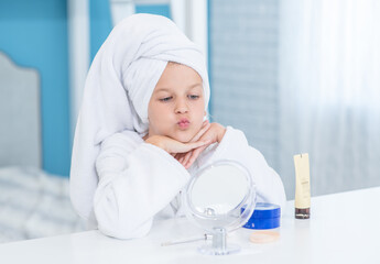 Happy little girl with a towel on her head looks in the mirror