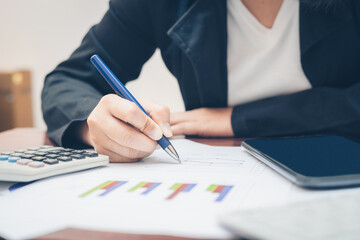 top view business woman working on table using pen point on business paper with financial accounting with growth statistics chart and graph for business analysis with calculator and tablet.