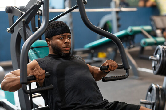 Motivated black guy having workout on chest press machine